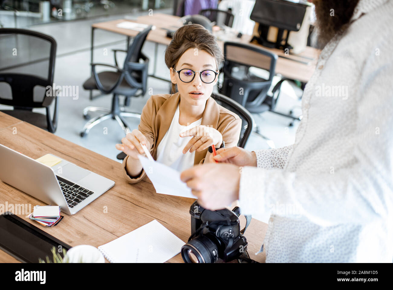 Two young colleagues talking at the working place, solving some working moments in the office or coworking space Stock Photo