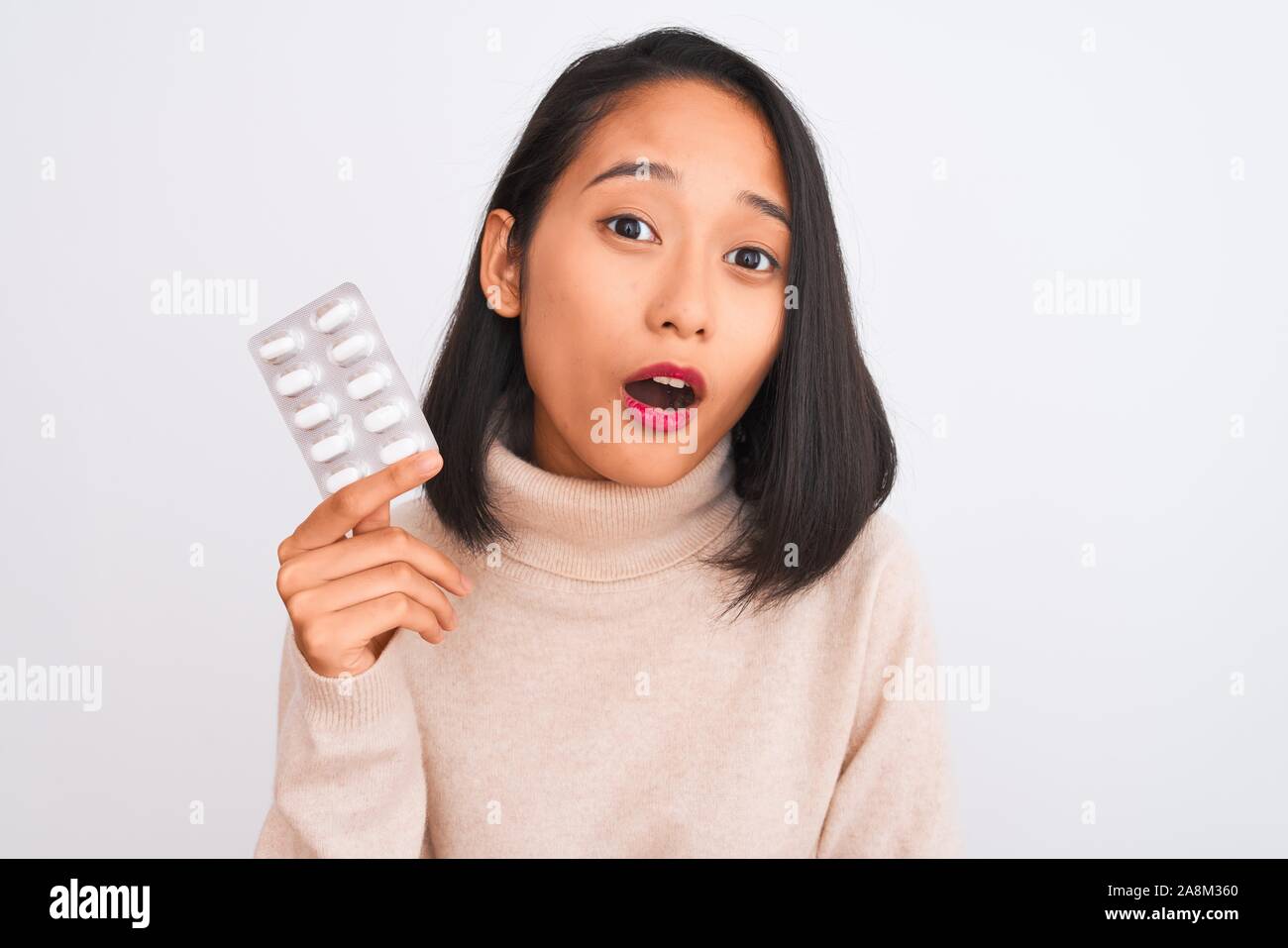 Young beautiful chinese woman holding pills standing over isolated