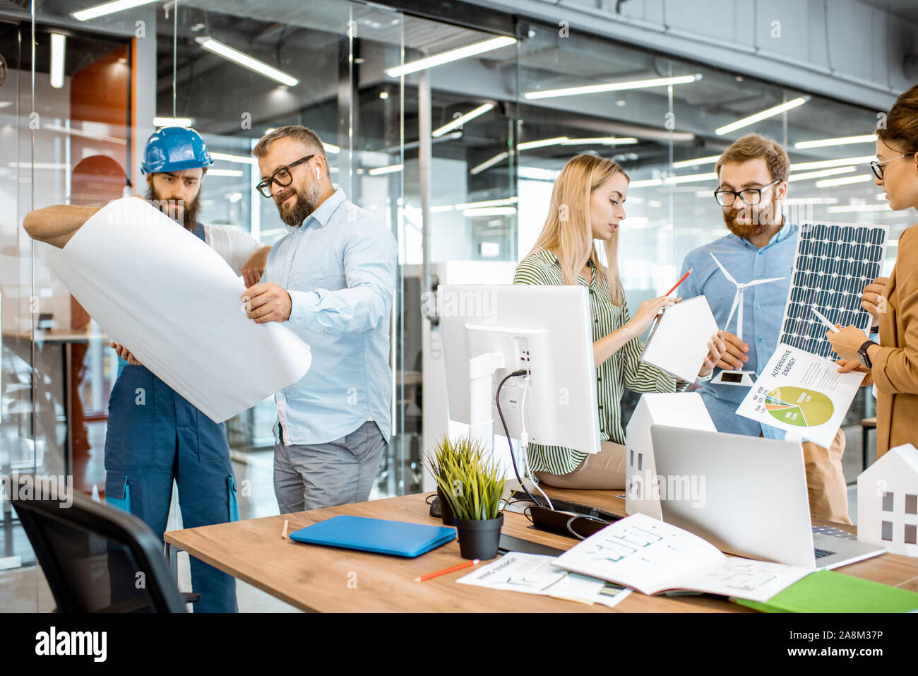 Group of young engineers working on a project of alternative energy, senior foreman and worker standing with blueprints in the office Stock Photo