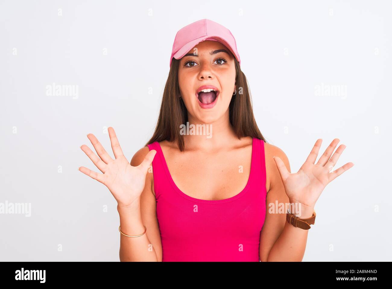 Young beautiful girl wearing pink casual t-shirt and cap over isolated white background celebrating crazy and amazed for success with arms raised and Stock Photo