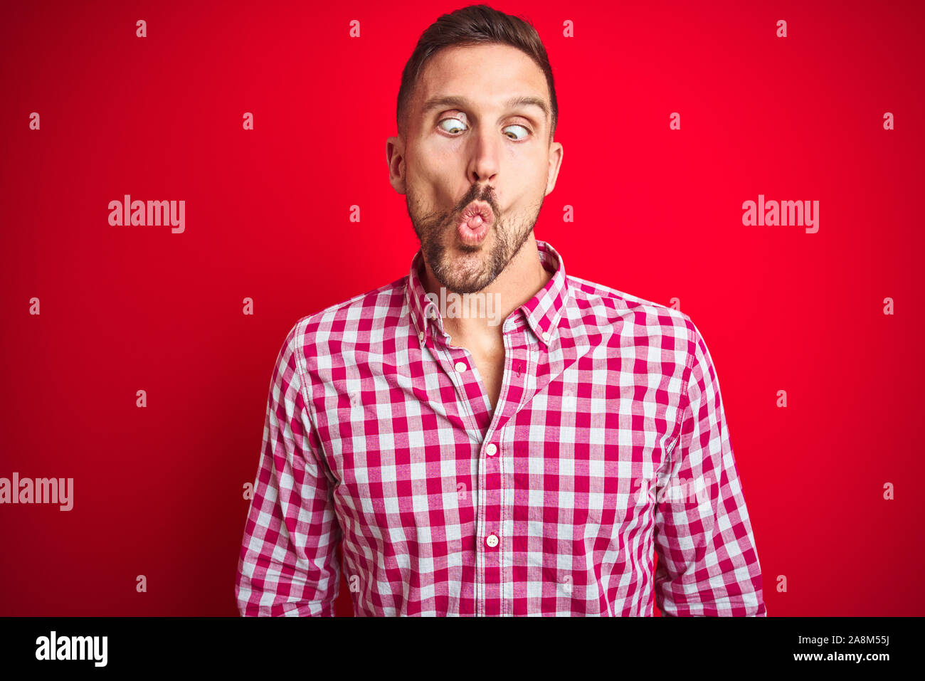 Young handsome man over red isolated background making fish face with ...