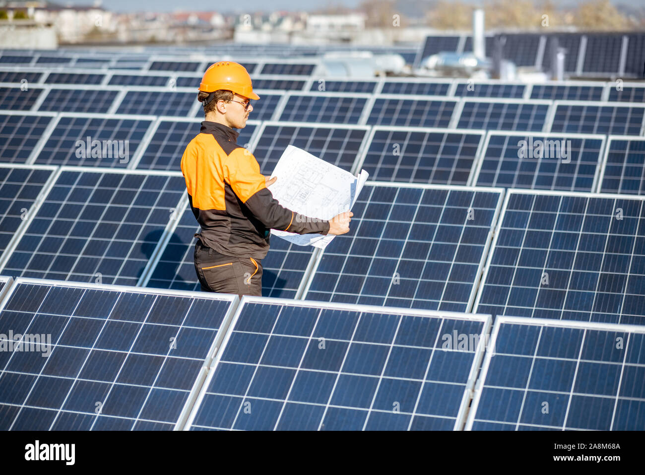 Engineer in protective workwear with blueprints of solar station project on a photovoltaic rooftop plant. Concept of designing power plants Stock Photo