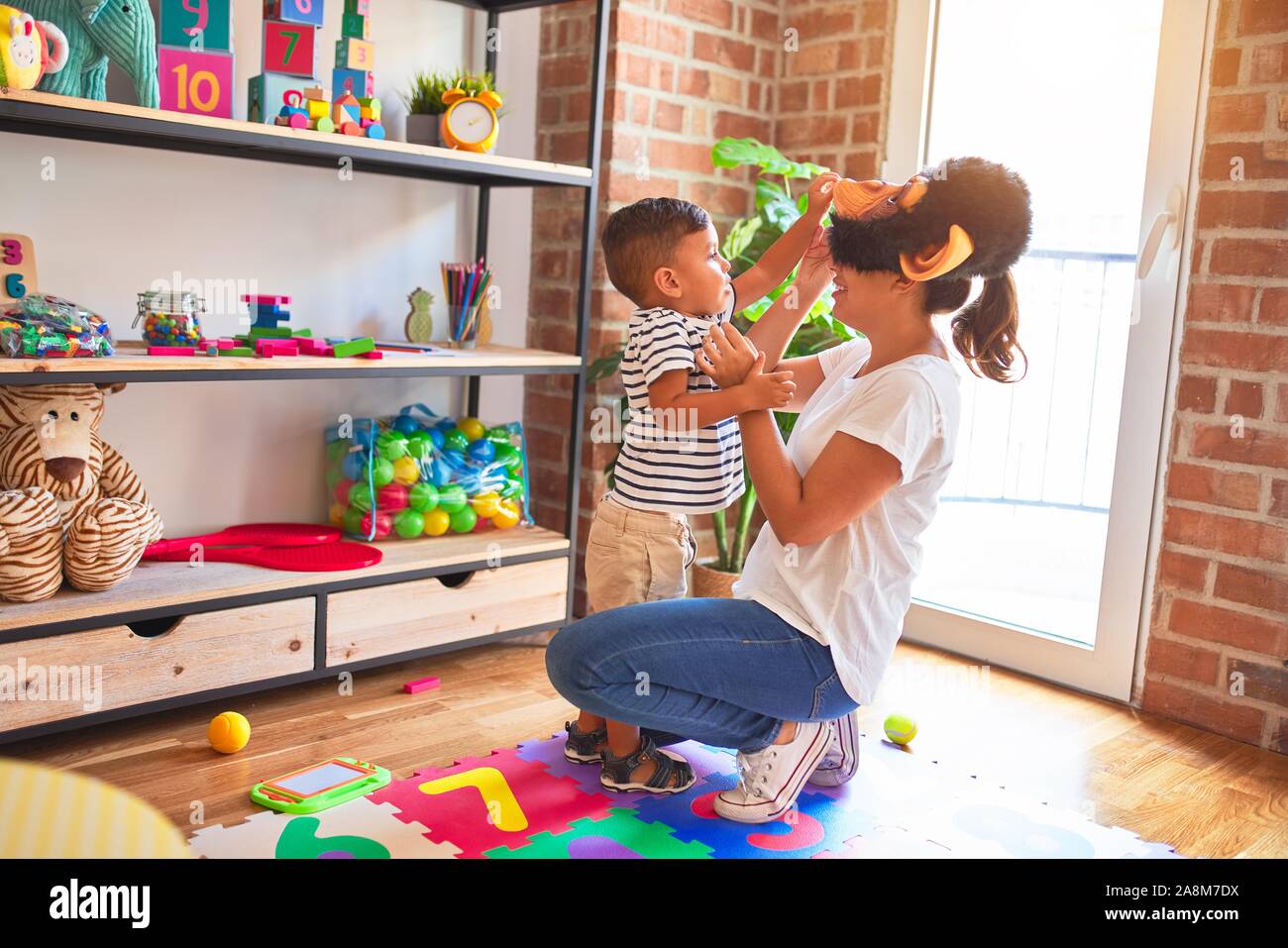 Beautiful teacher and toddler boy playing, woman with monkey mask at kindergarten Stock Photo