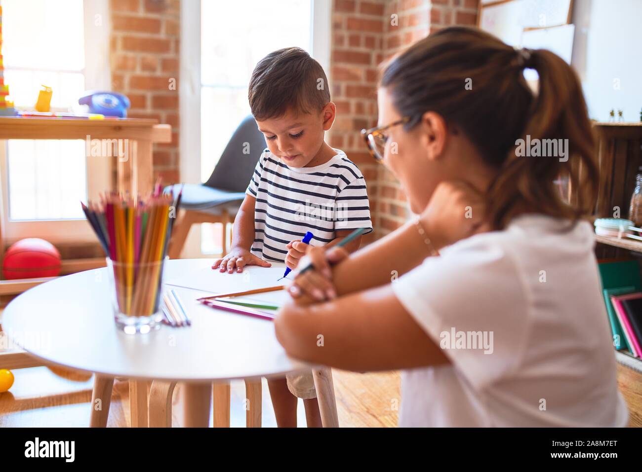 Beautiful teacher and toddler boy drawing draw using colored pencils at ...