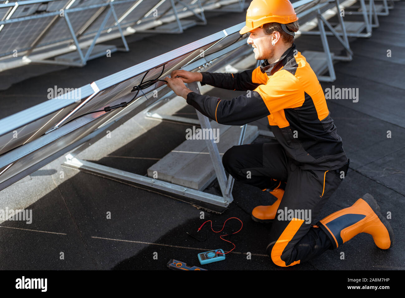 Well-equipped electrician connecting wires of solar panels on a rooftop photovoltaic power plant. Concept of installing solar stations Stock Photo