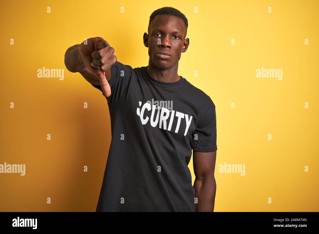 African american safeguard man wearing security uniform over isolated yellow background looking unhappy and angry showing rejection and negative with Stock Photo