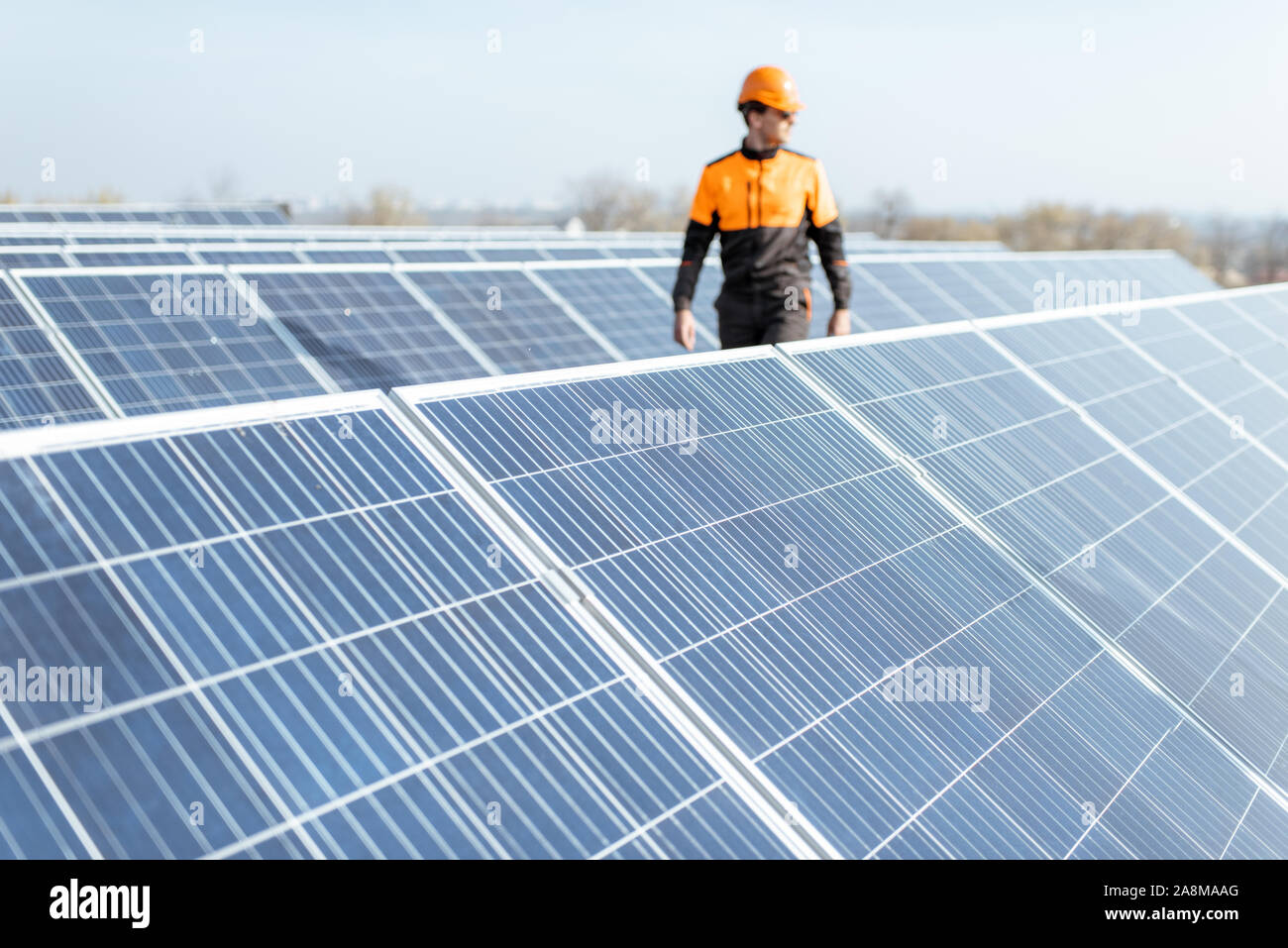 View on the rooftop solar power plant with engineer in protective workwear walking and examining photovoltaic panels. Concept of alternative energy and its maintenance Stock Photo