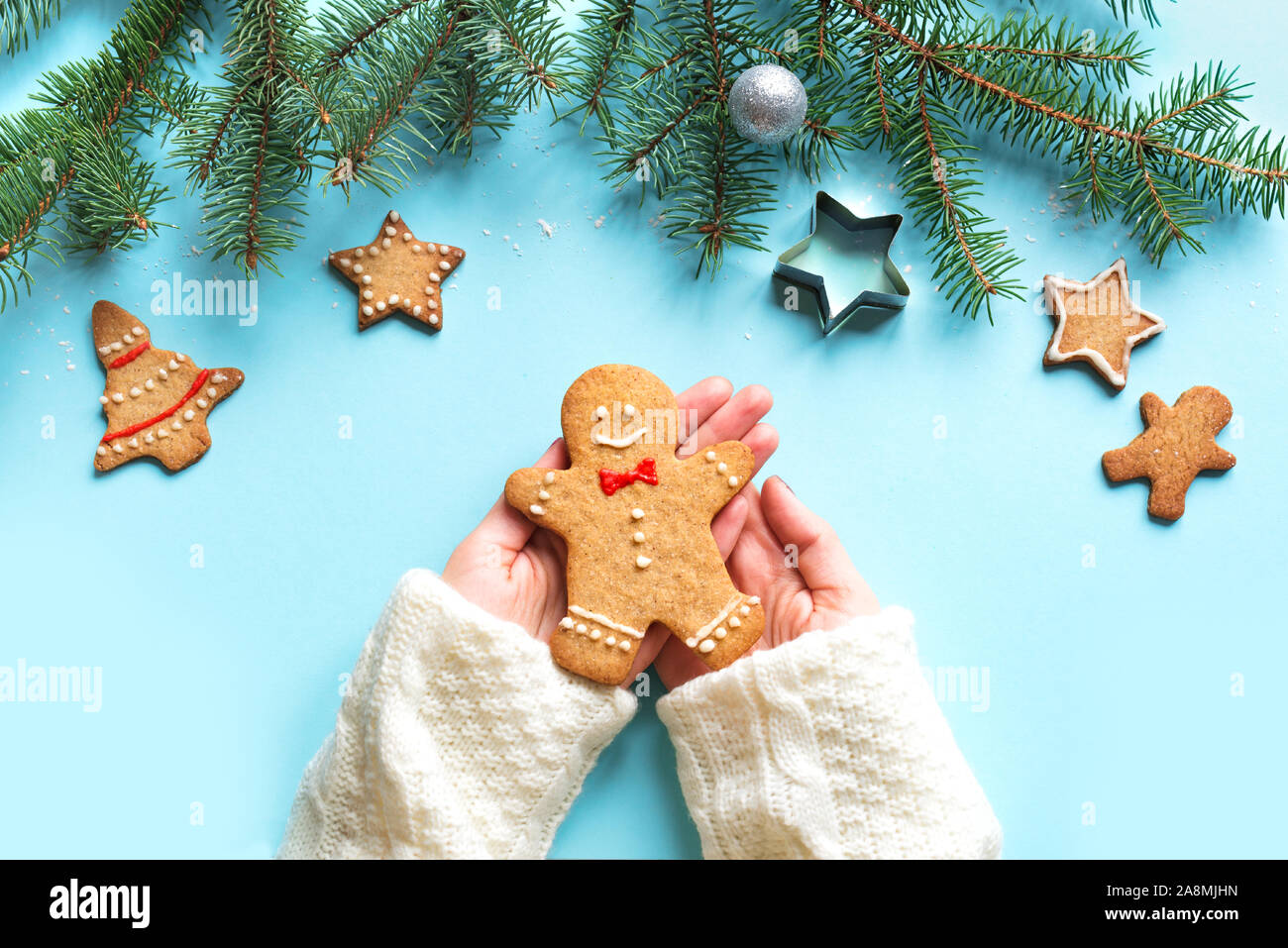 Gingerbread man in hands on blue background. Trendy Christmas minimal composition - hand holding homemade gingerbread man cookie, top view. Stock Photo
