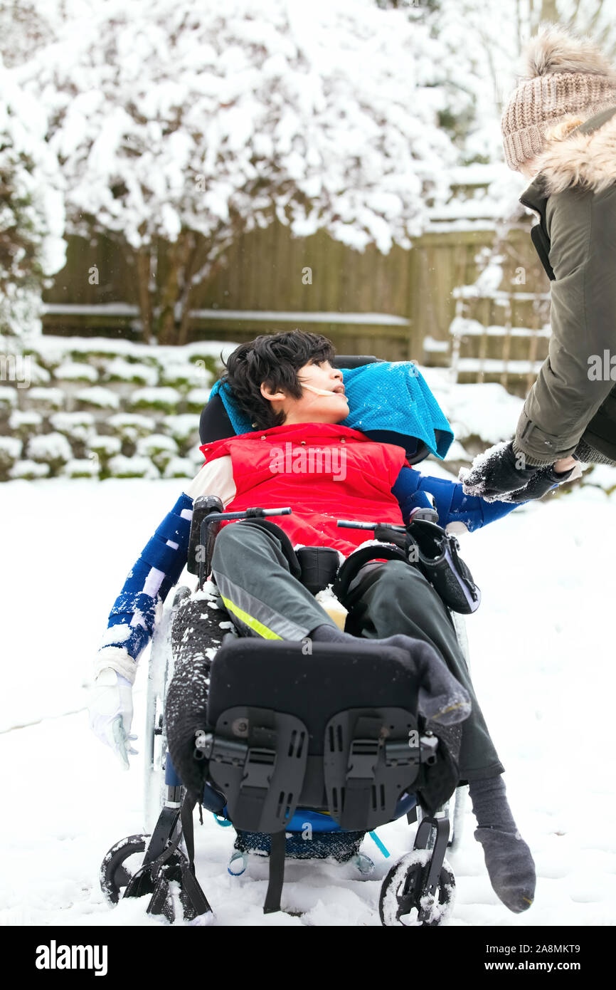 Little disabled boy in wheelchair outside playing with snow in winter Stock Photo