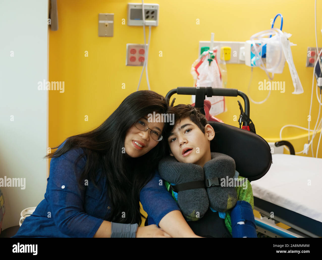 Smiling mother sitting next to disabled son in wheelchair by hospital ...