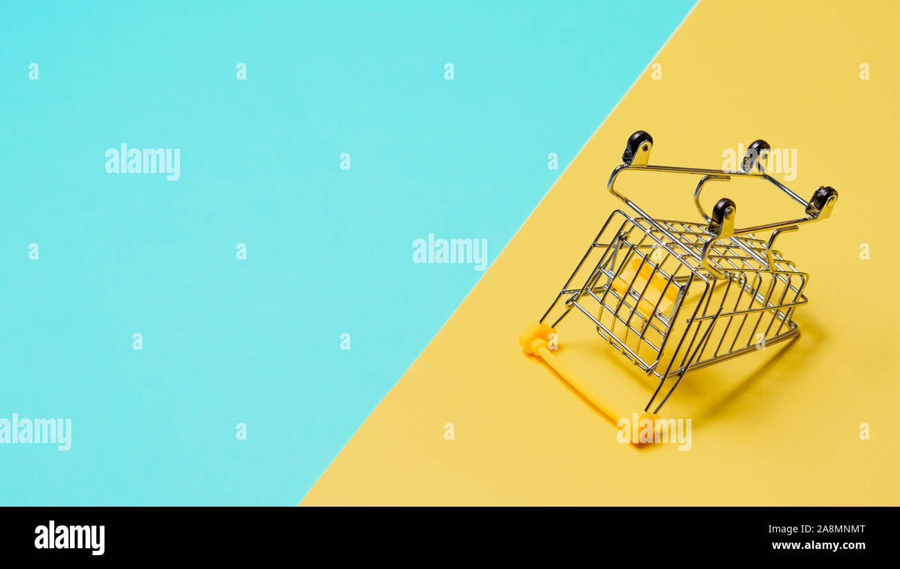 Empty inverted shopping cart on blue and yellow background. Inverted toy trolley on bright colorful background, copy space for text or design. Stock Photo