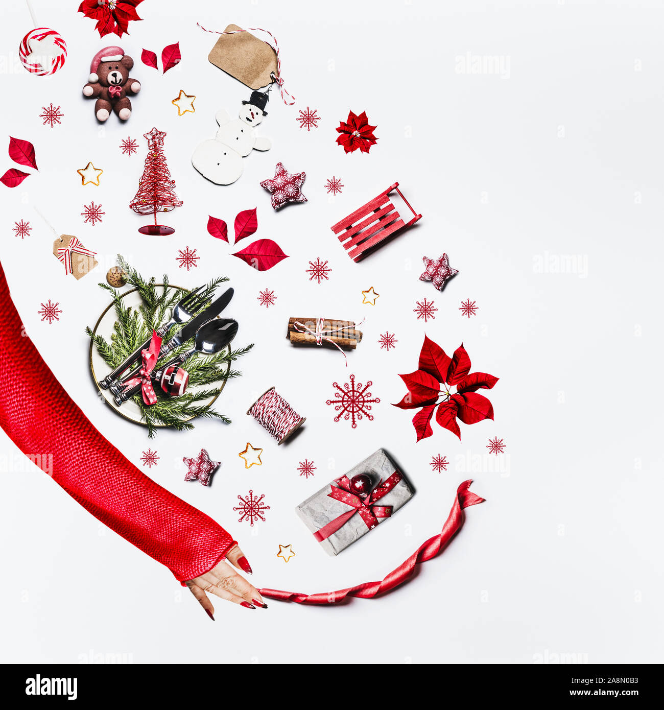 Woman hand in red sweater and various Christmas objects on white background, top view. Flat lay of Christmas table setting, holiday decoration and gif Stock Photo