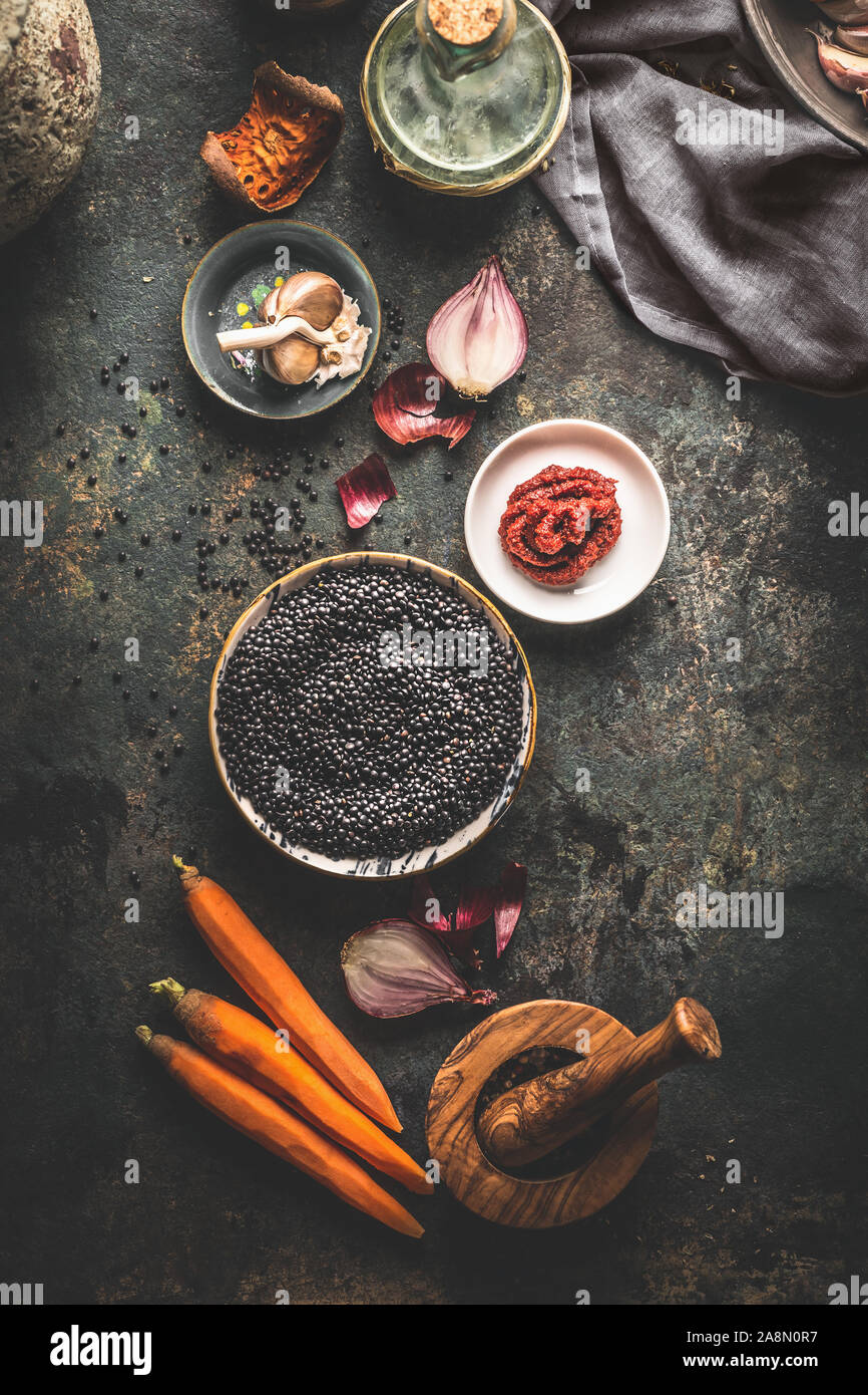 Black lentils with cooking ingredients for tasty vegan dishes on dark background. Top view. Healthy vegetarian eating concept. Horizontal banner. Plan Stock Photo