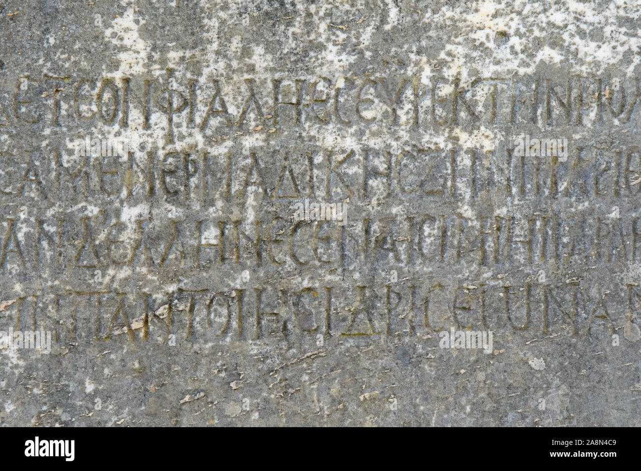 Half-erased ancient Greek letters embossed on an old gray marble slab covered with cracks and mold. Stock Photo