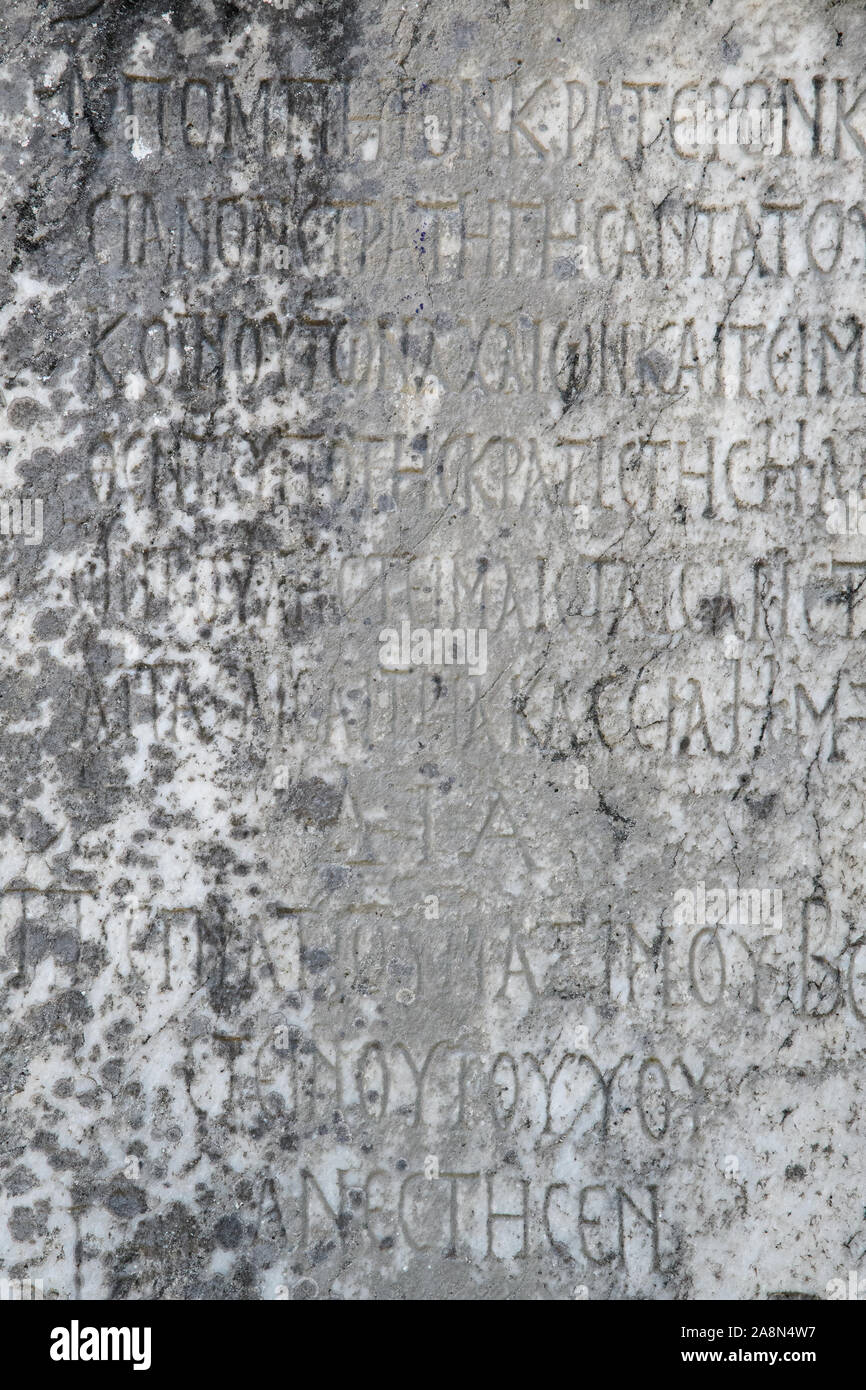 Half-erased ancient Greek letters embossed on an old gray marble slab covered with cracks and mold. Stock Photo