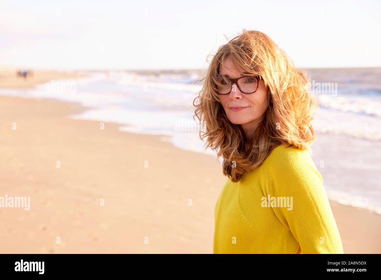 Close-up portrait of beautiful smiling mature woman with frizzy hair walking on the beach and enjoying sunrise. Stock Photo
