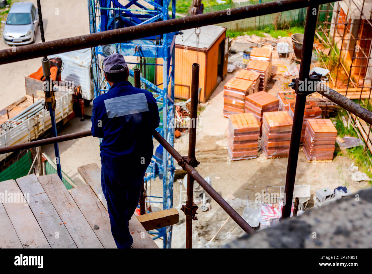 Rigger is standing on scaffold with wooden platform high up on scaffold