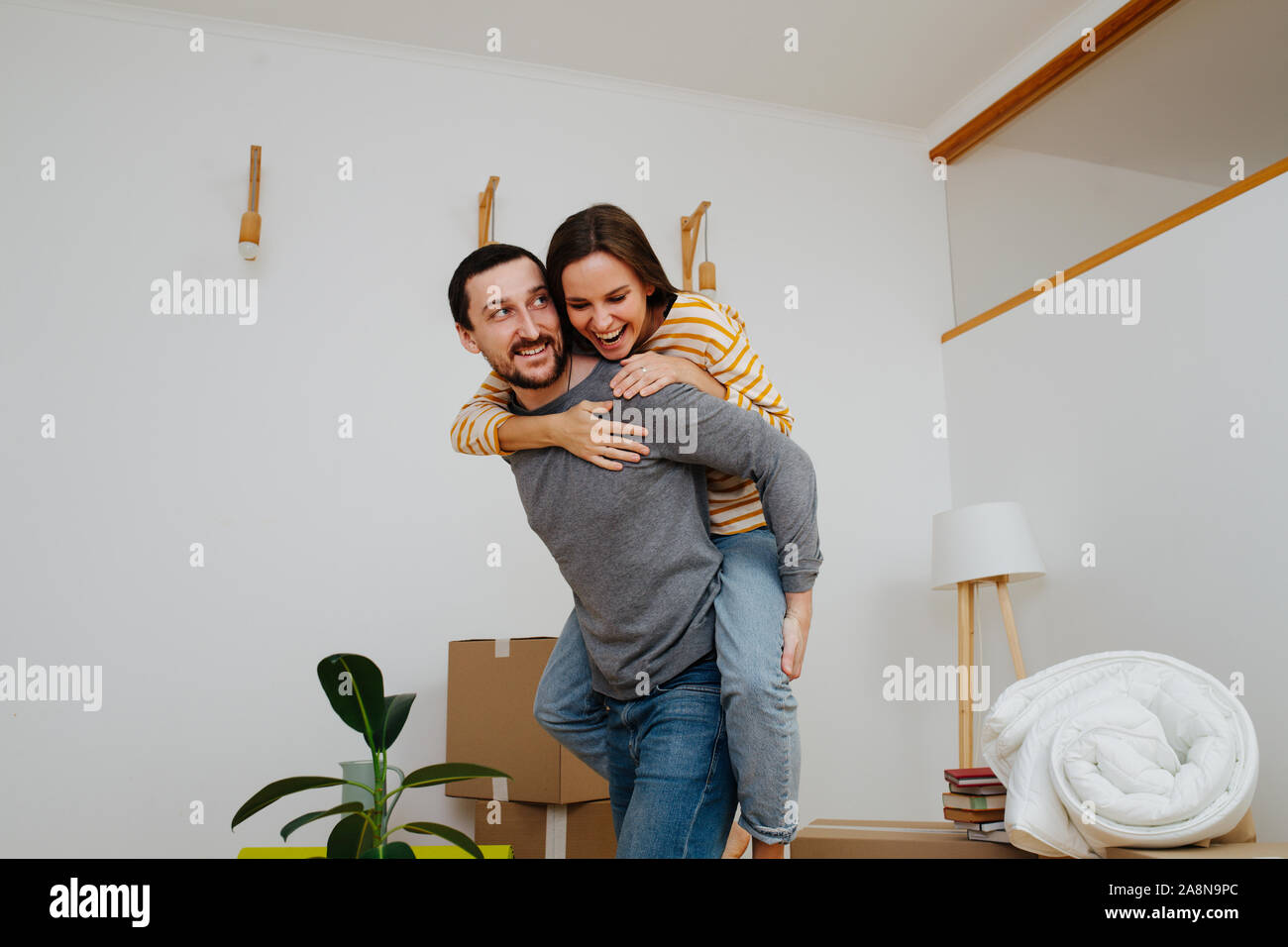 Couple celebrating moving into a new apartment. Woman riding on her man's back. Stock Photo