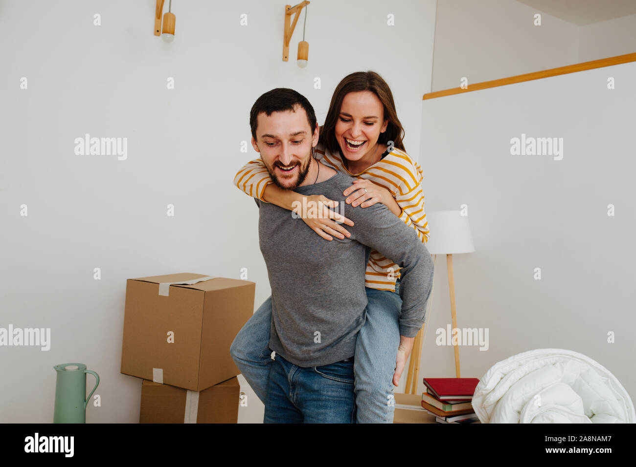Couple celebrating moving into a new apartment. Woman riding on her man's back. Stock Photo