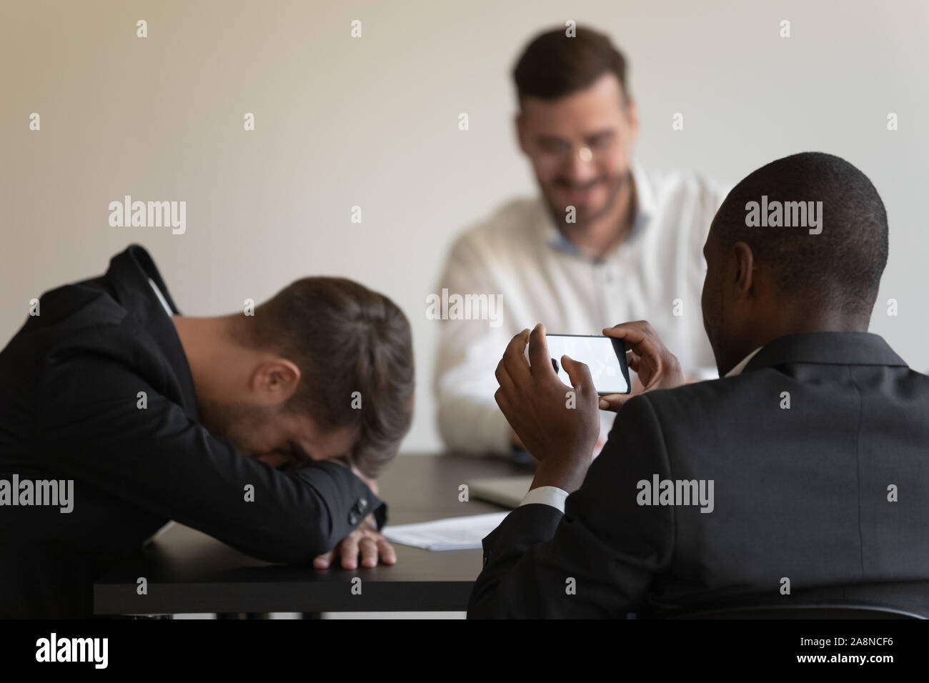 Employees take pictures of sleeping coworker at team meeting Stock Photo