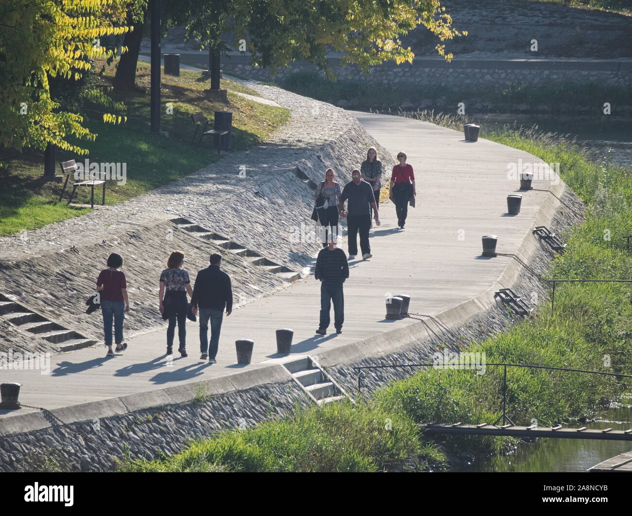 People Walking on Riverside Promenade at Rába River on a Sunny Autumn Day in Győr, Hungary Stock Photo