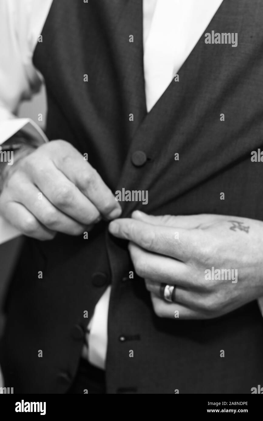 A man, groom putting on his braces, buckling them to his trousers on