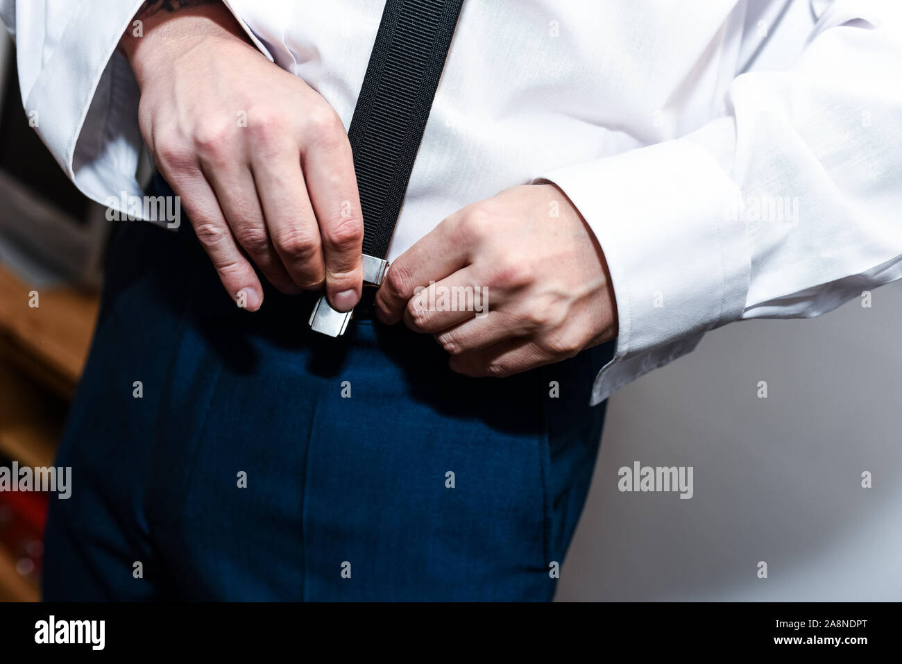 A man, groom putting on his braces, buckling them to his trousers on
