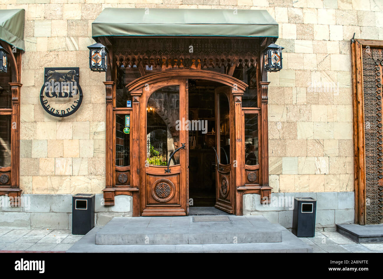 Gyumri,Armenia,05 September,2019: Entrance to the restaurant is through a double wooden door decorated with carved ornaments and a cornice in a buildi Stock Photo