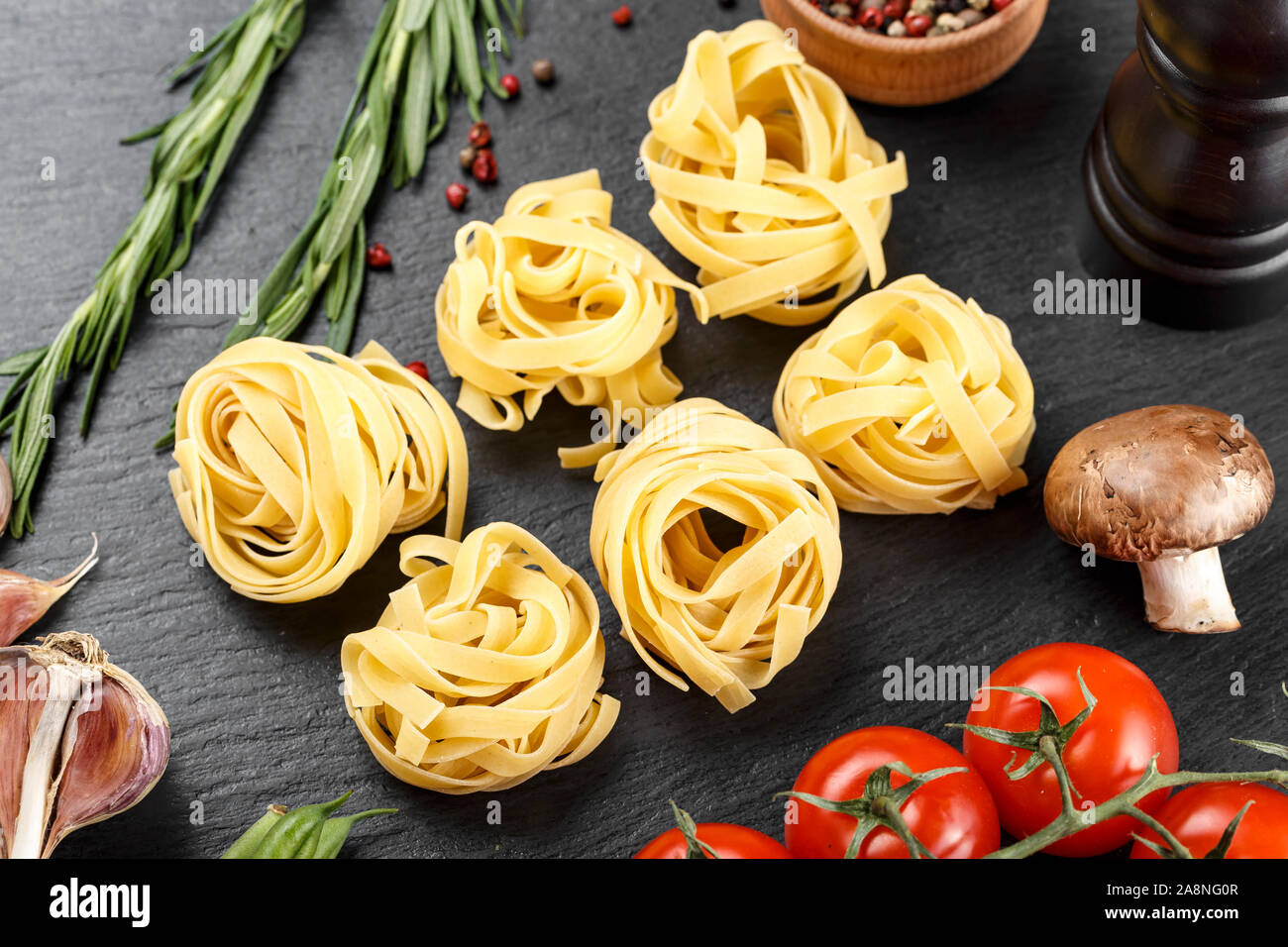 raw italian tagliatelli spaghetti on a black slate board with vegetables and spices. Stock Photo