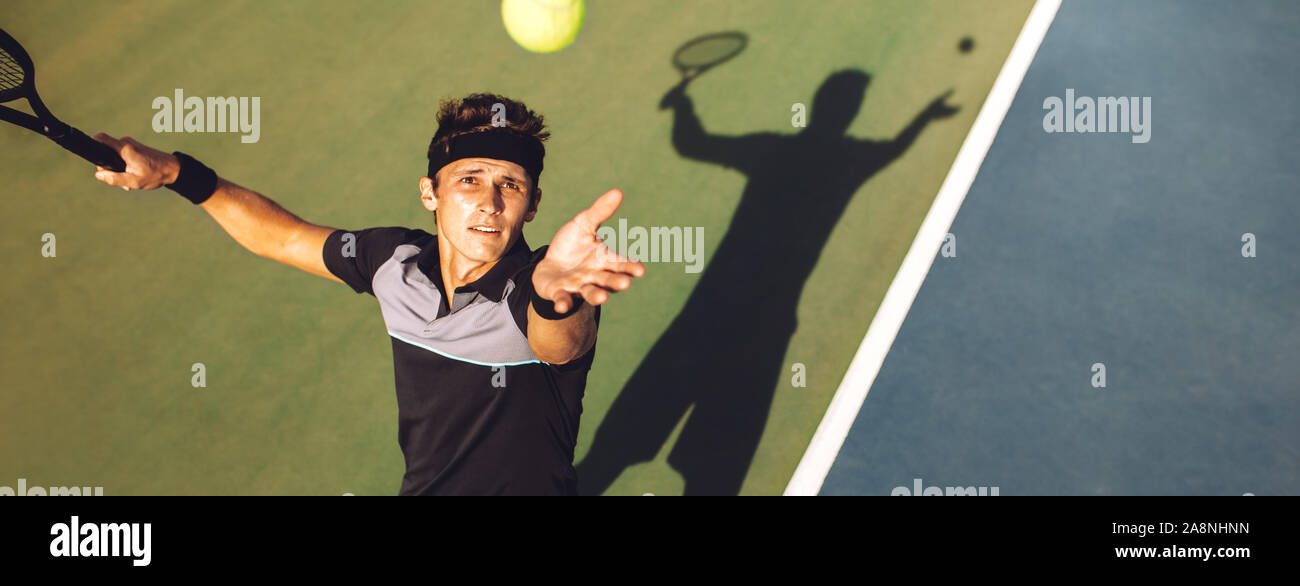 Top view of professional tennis player ready to hit the ball with the racket after tossing while serving in the beginning of a match. Stock Photo