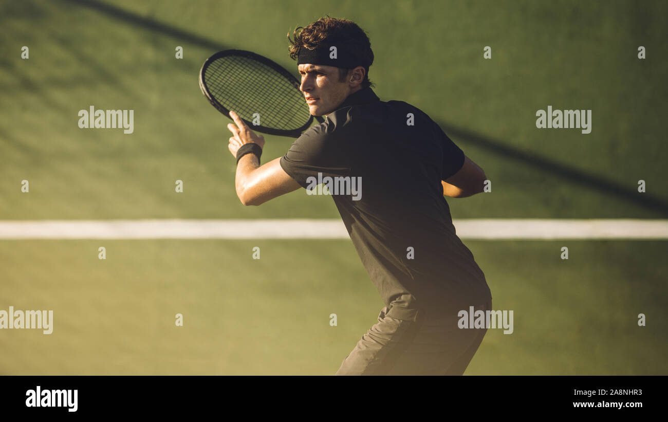 Young player playing tennis on hard court. Professional tennis player hitting a forehand during a match. Stock Photo