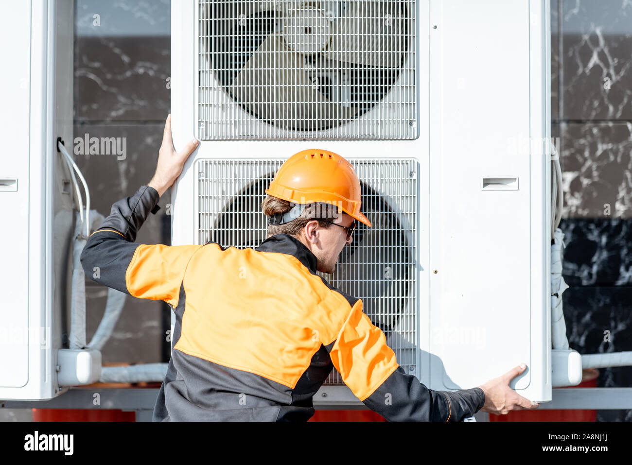 Professional workman in protective clothing installing outdoor unit of