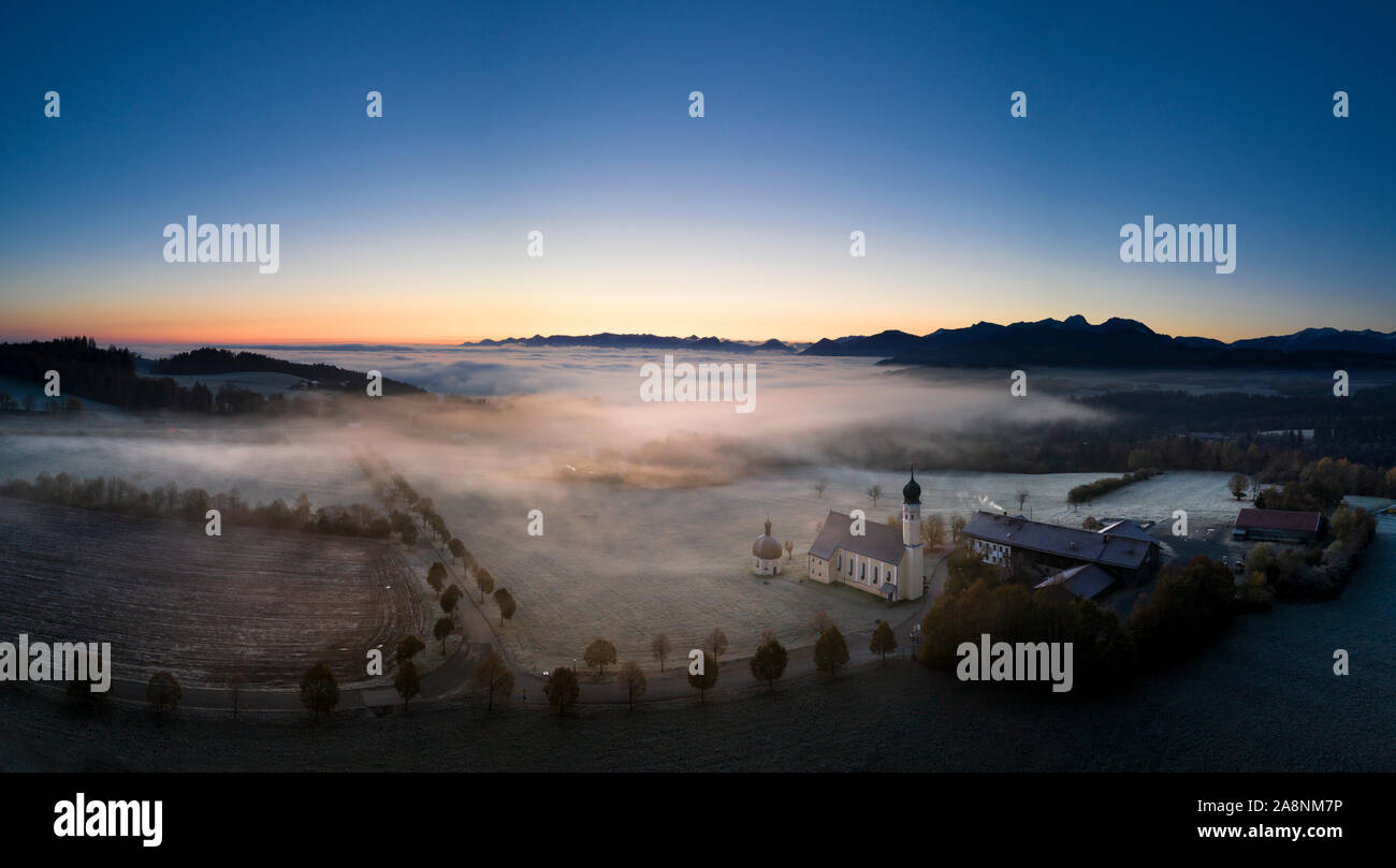 Beautiful foggy autumn morning in Bavaria - aerial view of Wilparting Church before Alps in Chiemgau Stock Photo