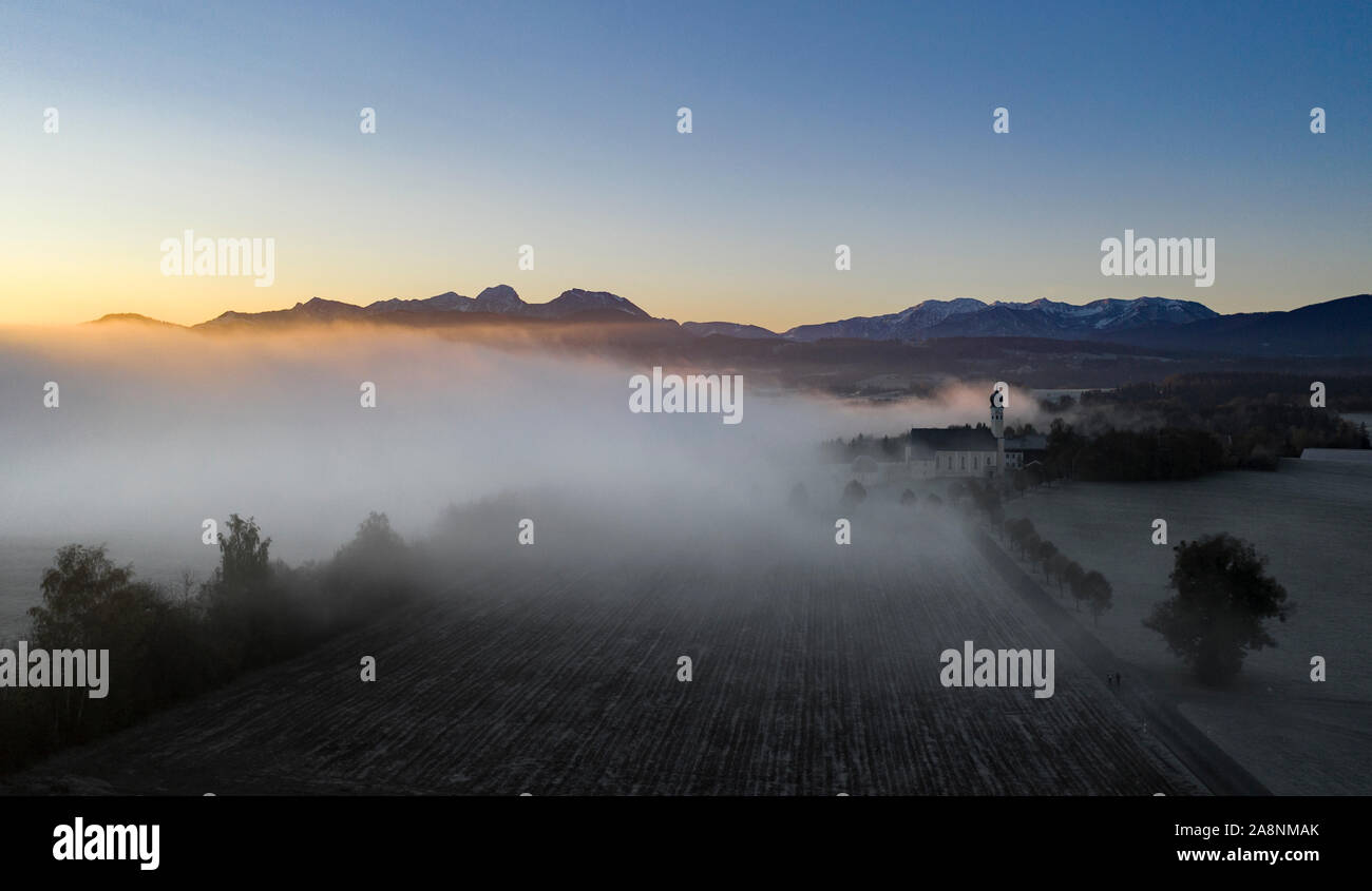 Beautiful foggy autumn morning in Bavaria - aerial view of Wilparting Church before Alps in Chiemgau Stock Photo