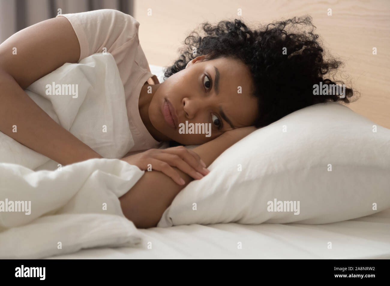 Unhappy African American woman suffering from insomnia, lying in bed Stock Photo