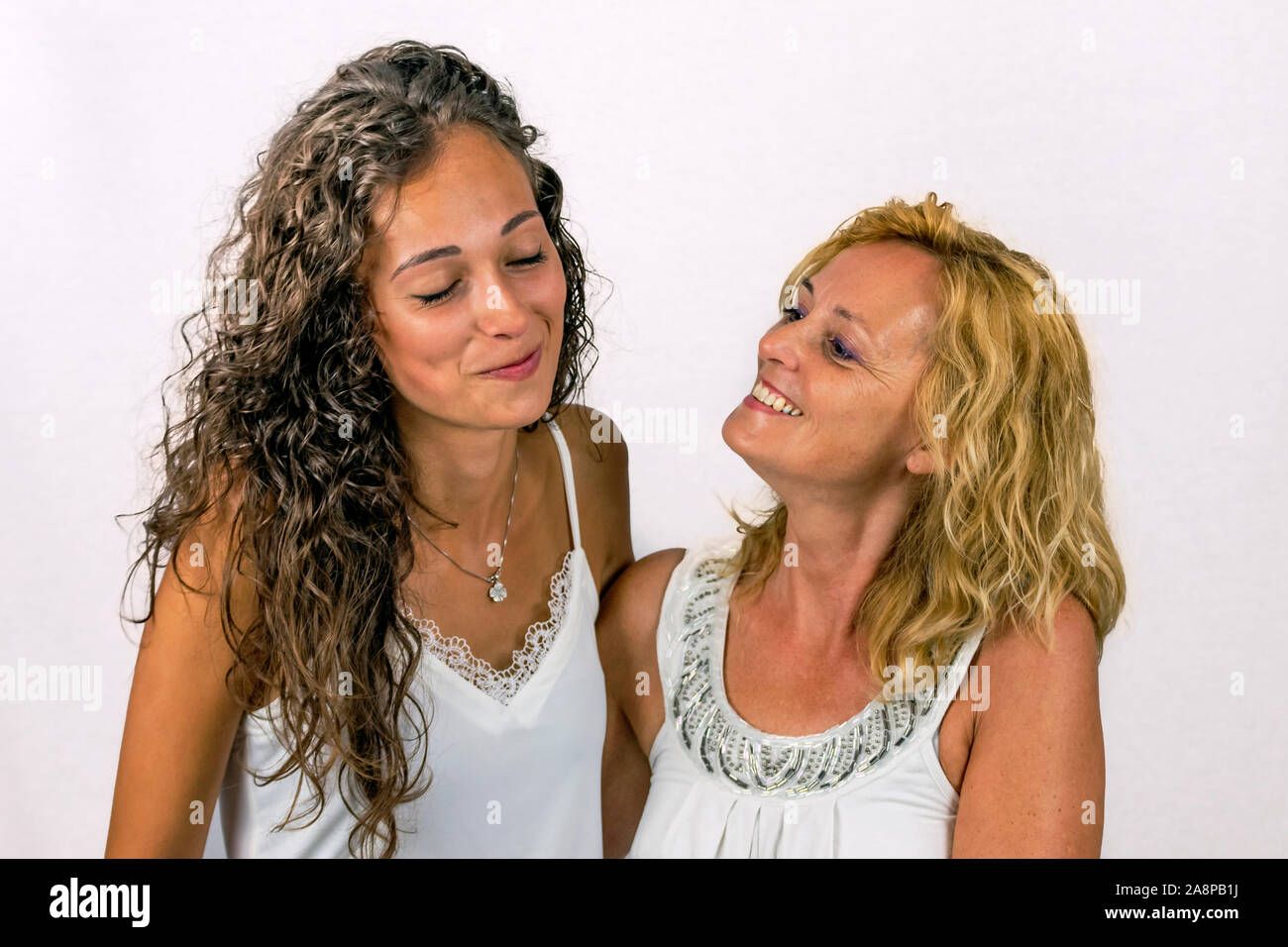Intense moment of complicity between mother and daughter dressed in white on a white background Stock Photo