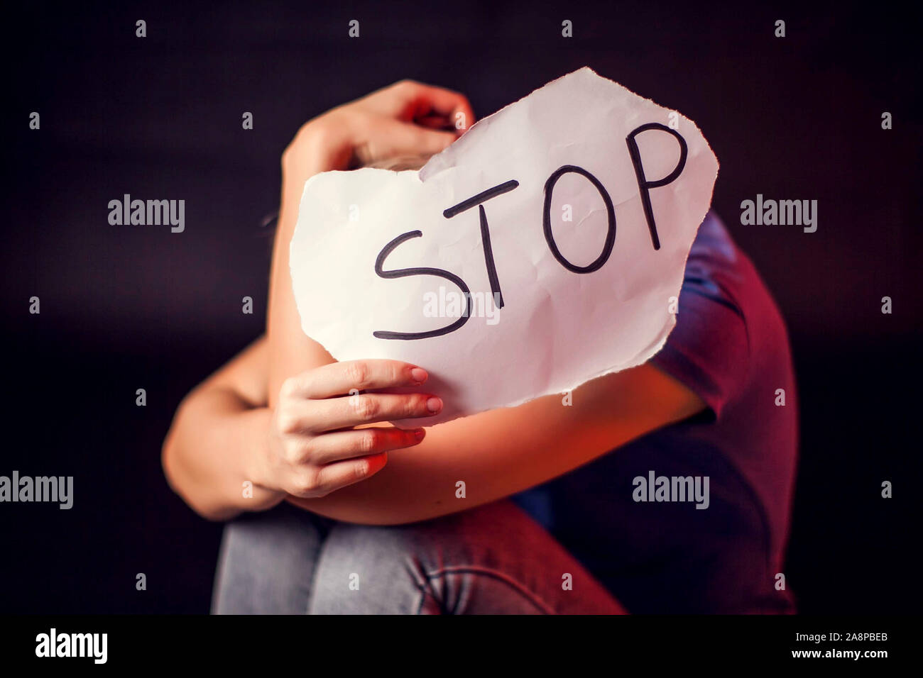 Woman holds paper with message to help her in front of black background. People, family violence, crime concept Stock Photo
