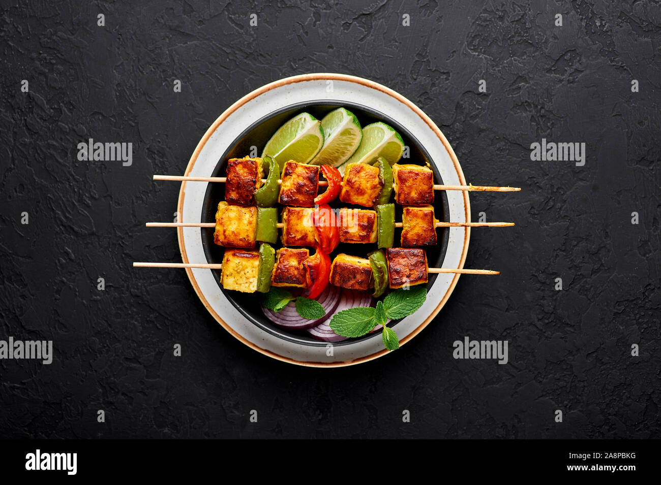 Paneer Tikka at skewers in black bowl at dark slate background. Paneer