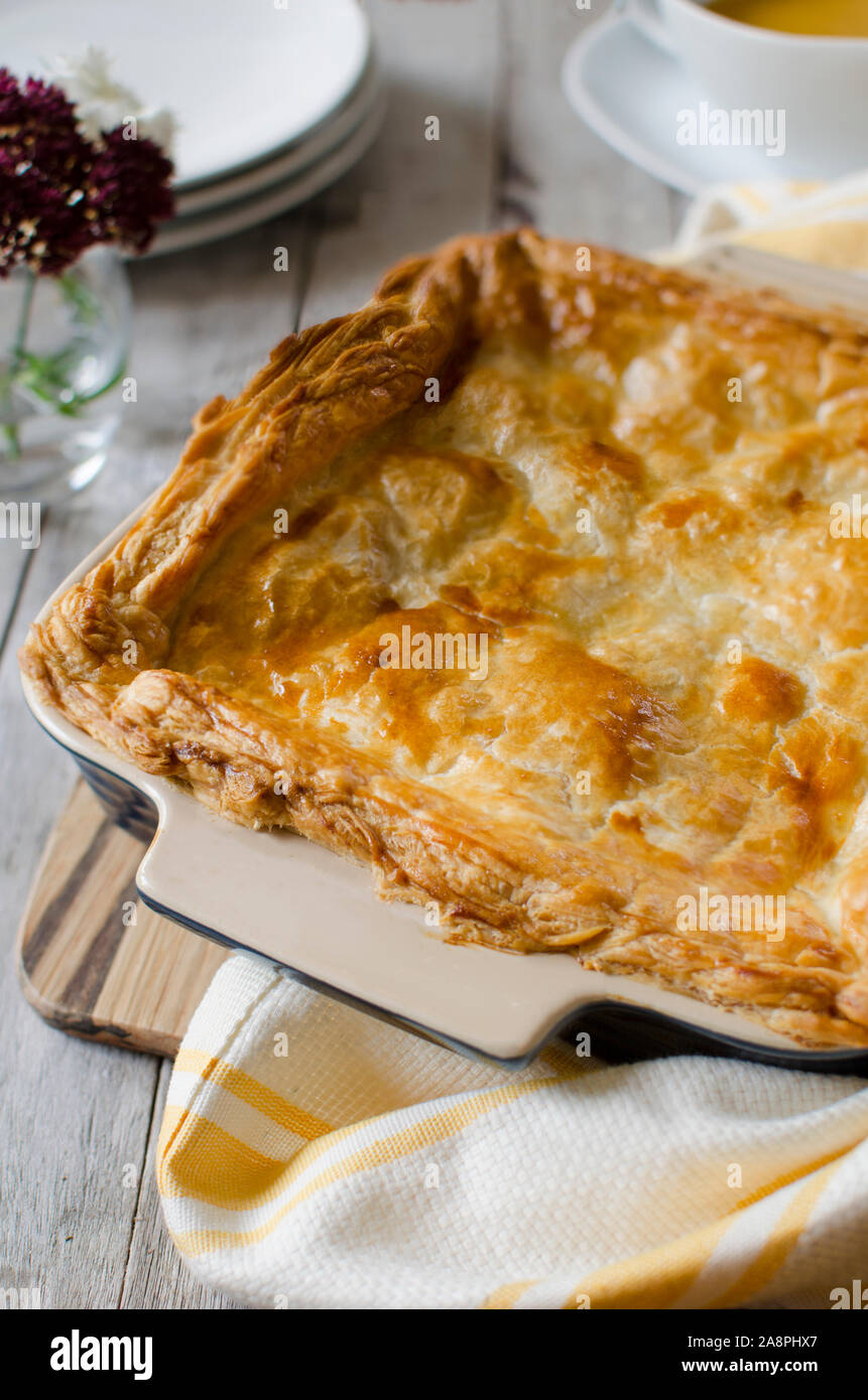 Above shot of pie with pie in baking tray, has flowers and tea towl as props, with a wooden background. Stock Photo