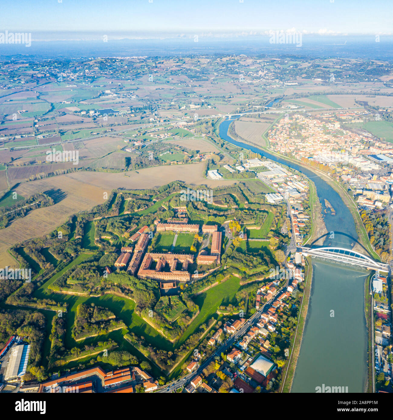 Aerial view of modern six-star hexagon shaped fort Cittadella of Alessandria on winding river Tanaro. Piedmont, Italy. Alps in the background. Bridge Stock Photo