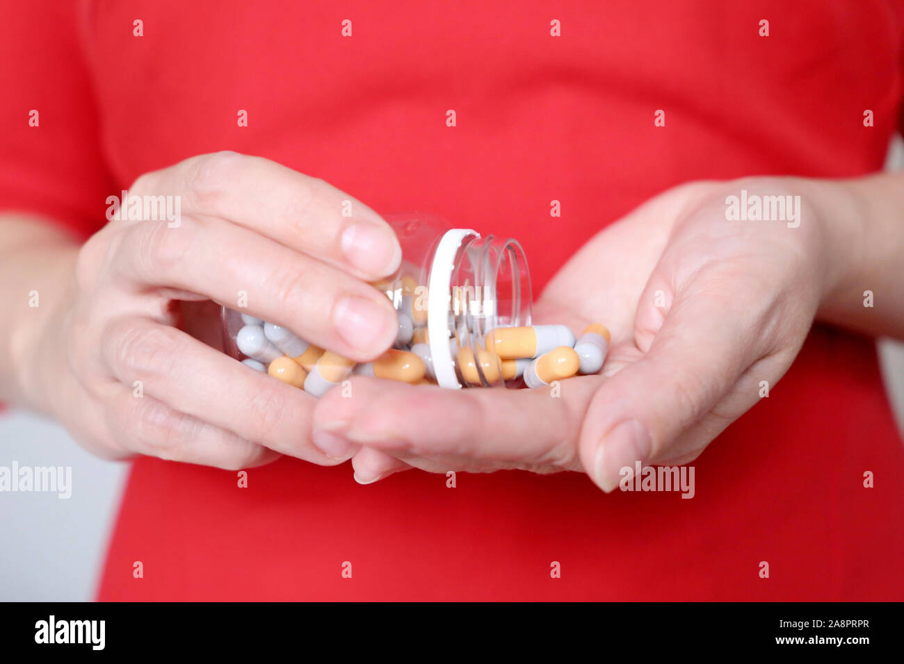 Pills in female hands, woman in red dress holding bottle of medical capsules. Concept of vitamins for beauty, skin care, taking medication,  diet pill Stock Photo