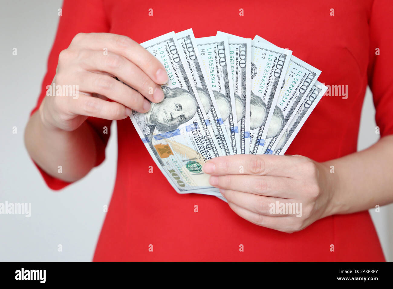 Woman in red dress holding US dollars in hands, close-up. Manager or businesswoman counts the money, concept of a salary, shopping, cash Stock Photo