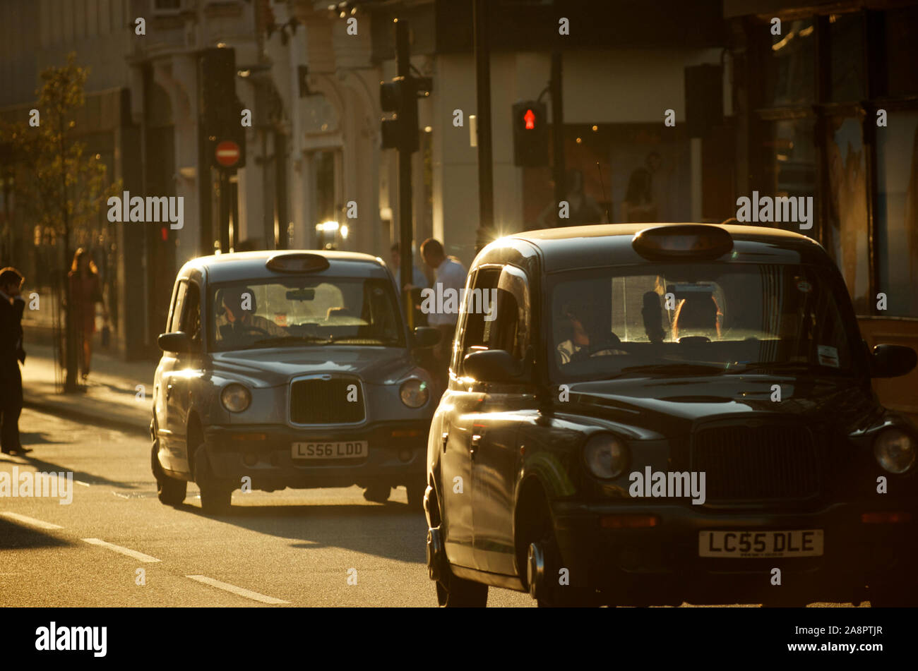 LONDON - SEPTEMBER 30, 2011: A pair of black taxis, also known as Hackney Carriages, drive in afternoon sun. Stock Photo