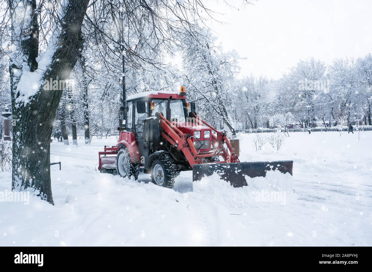 A red old tractor clears the street of snow in a snow storm. Street cleaning in winter. Stock Photo