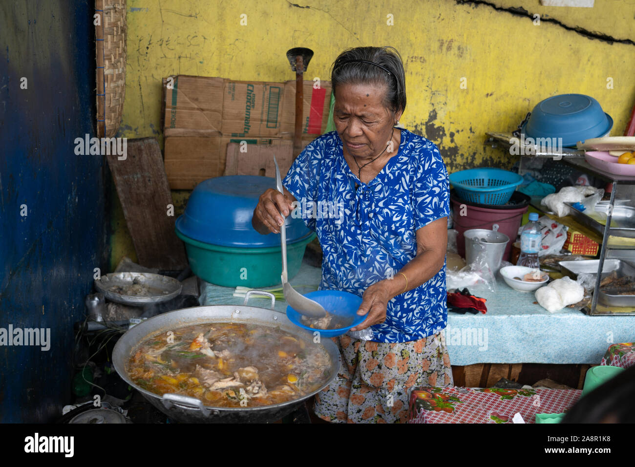 A Filipino woman serving a bowl of stewed fish from a large cooking wok