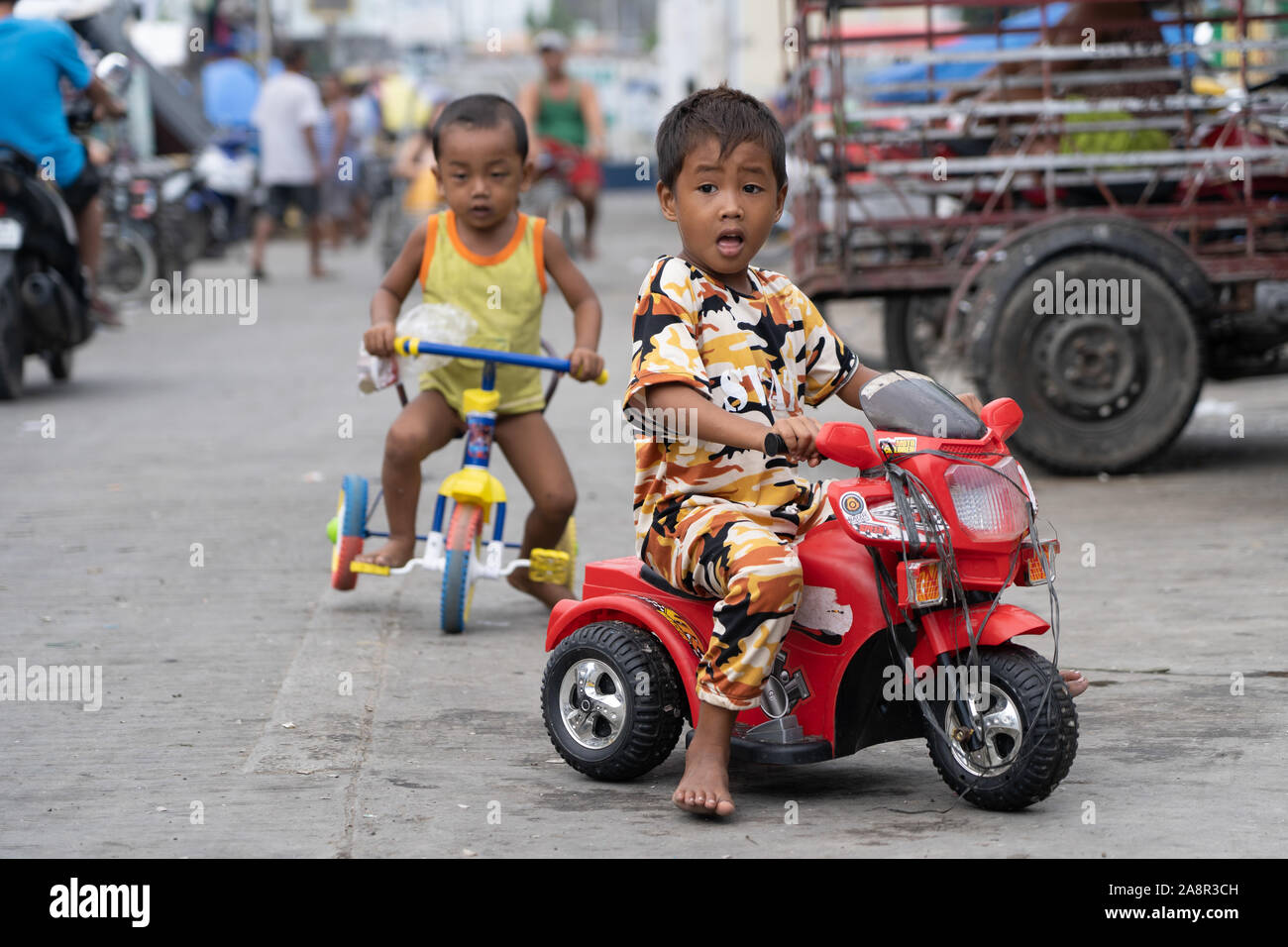 Two young Filipino boys playing in a poor area of Cebu City riding toy tricycles. Stock Photo