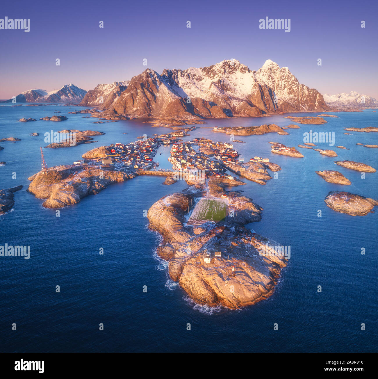 Aerial view of rocks in sea, snowy mountains, purple sky Stock Photo