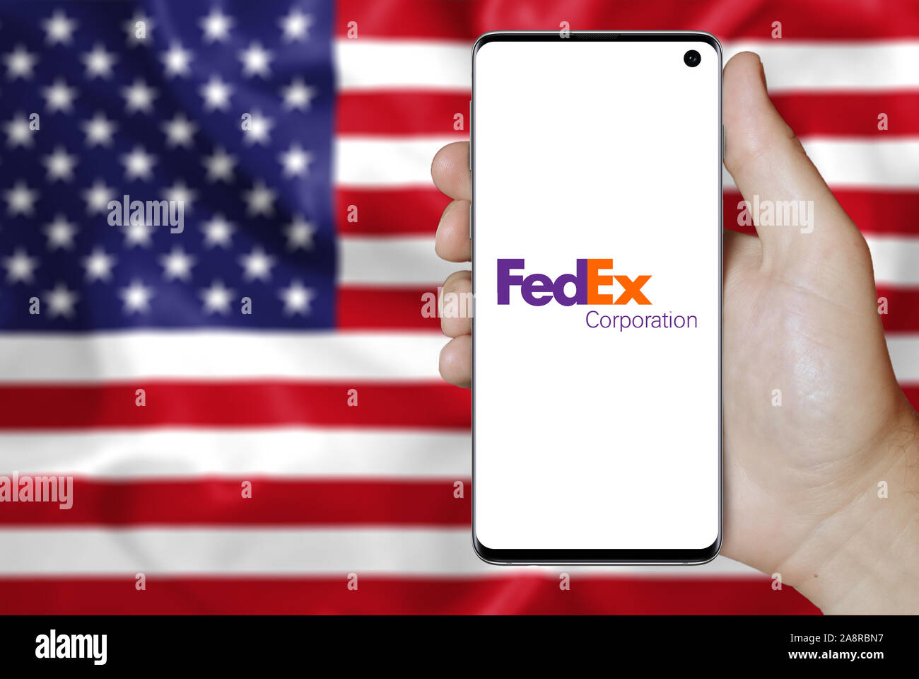 Logo of public company FedEx Corporation displayed on a smartphone. Flag of USA background. Credit: PIXDUCE Stock Photo