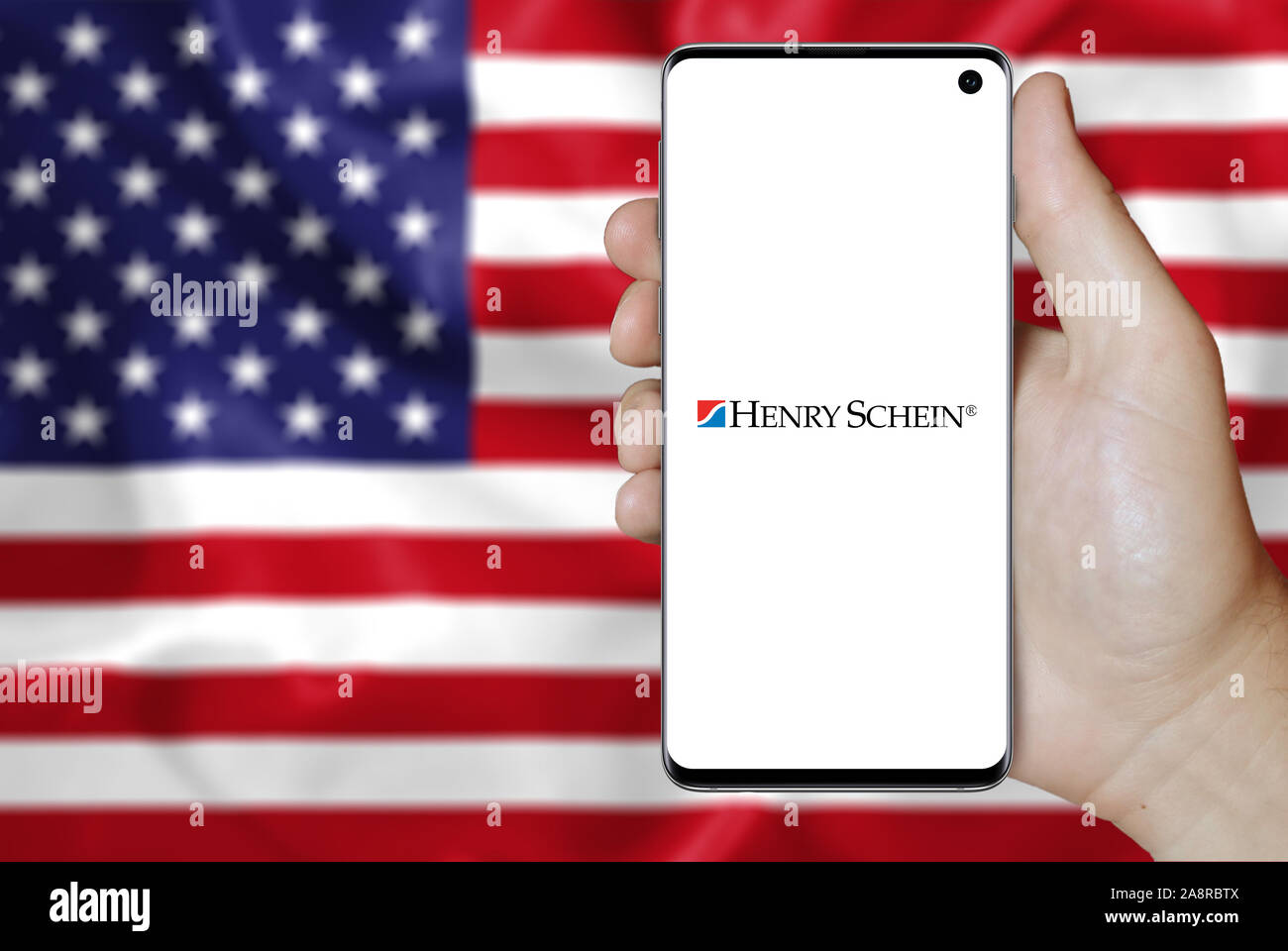 Logo of public company Henry Schein displayed on a smartphone. Flag of USA background. Credit: PIXDUCE Stock Photo