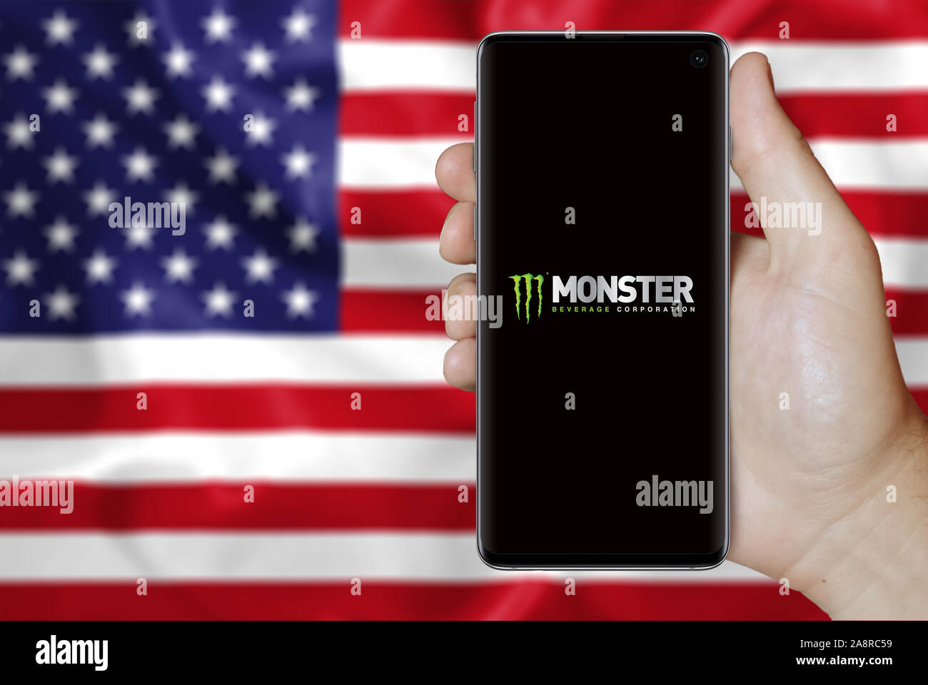 Logo of public company Monster Beverage displayed on a smartphone. Flag of USA background. Credit: PIXDUCE Stock Photo